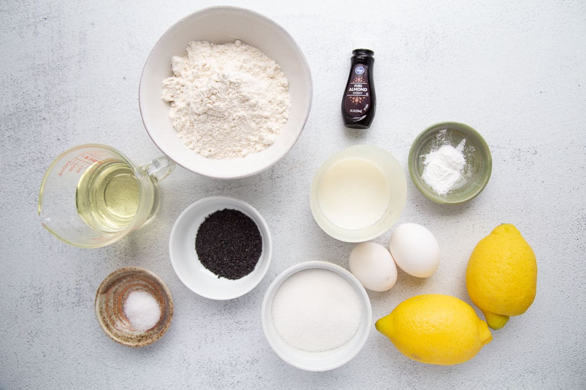 flour, lemons, almond extract, and more ingredients on a white table.