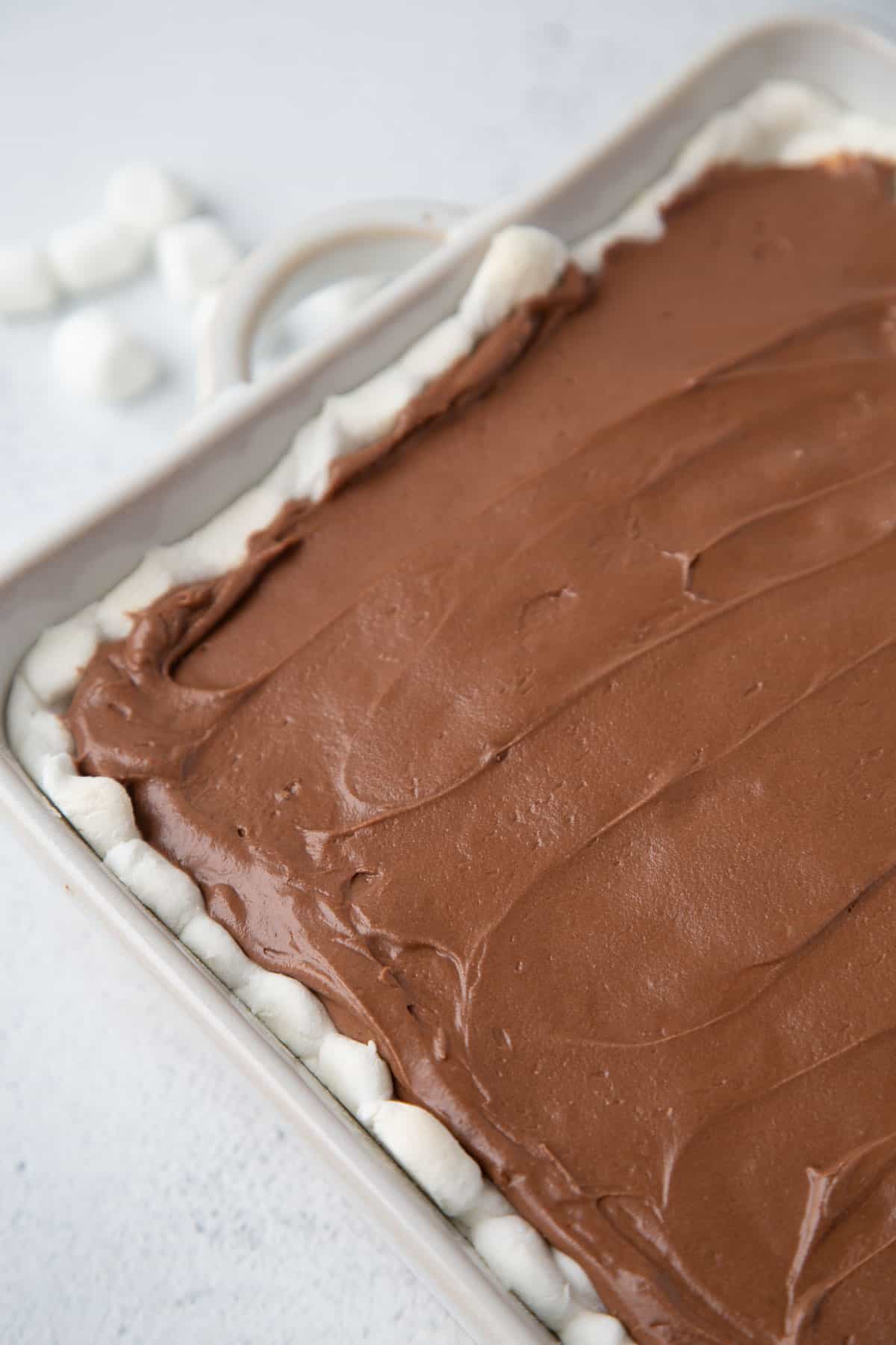 chocolate frosting on top of a cake with marshmallows on the edges.