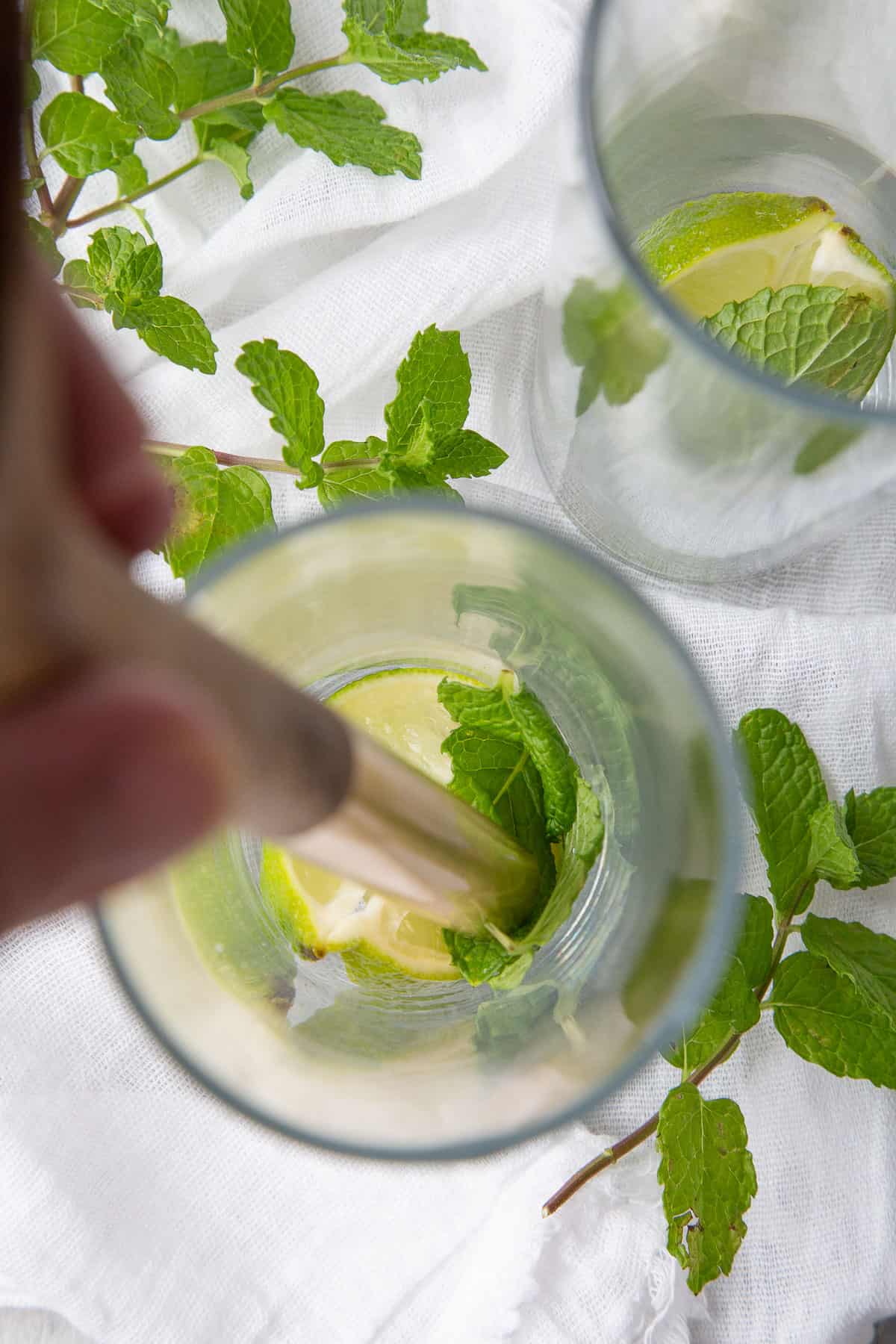 wooden spoon muddling limes and mint leaves.
