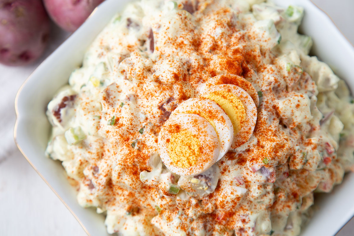 red potato salad in a white dish, topped with a hard boiled egg and paprika.