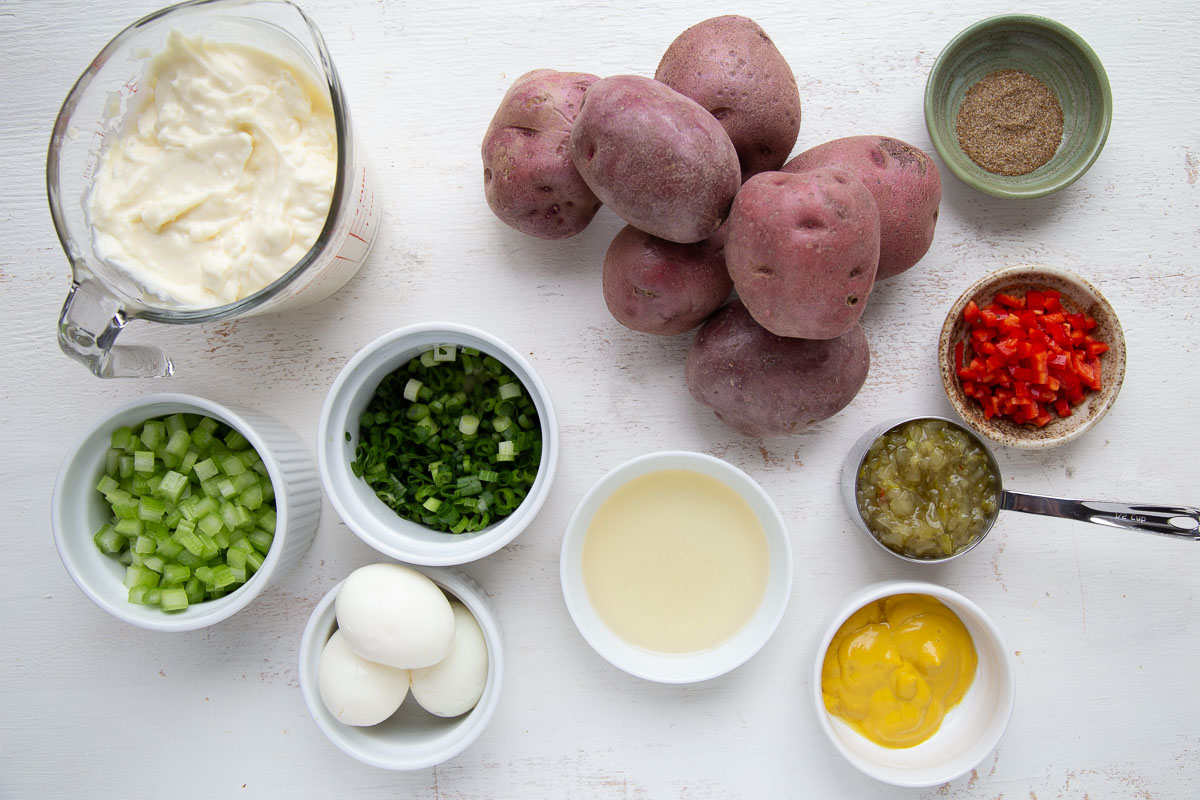 red potatoes, green onions, mayo, and other ingredients on a white table.