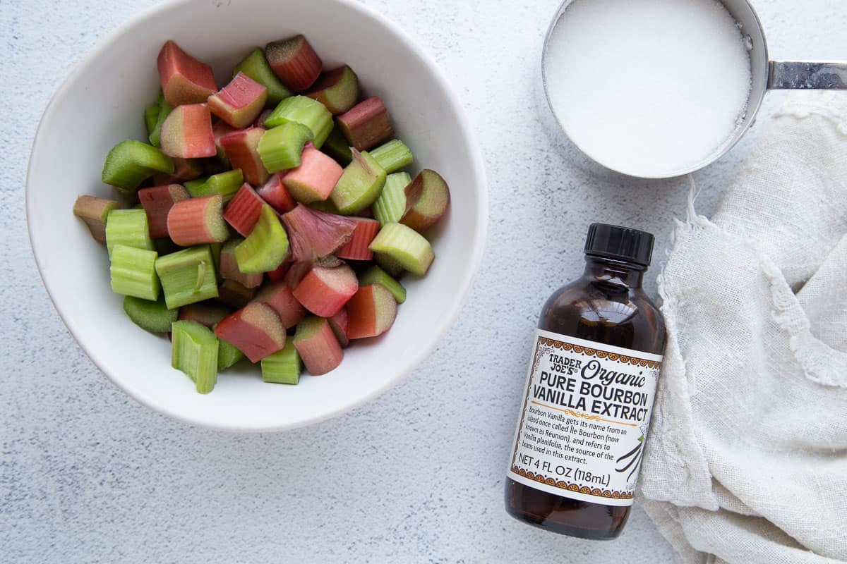 rhubarb, sugar, and vanilla extract on a white table.