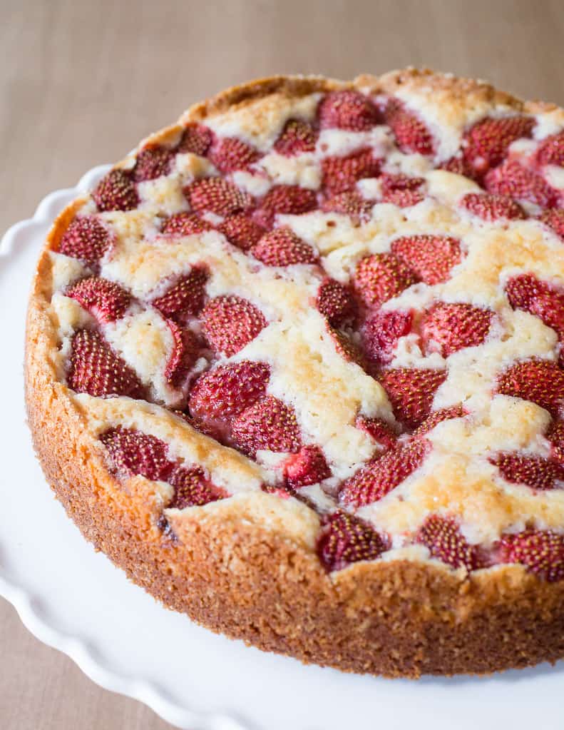 strawberry cake topped with strawberries on a white platter.