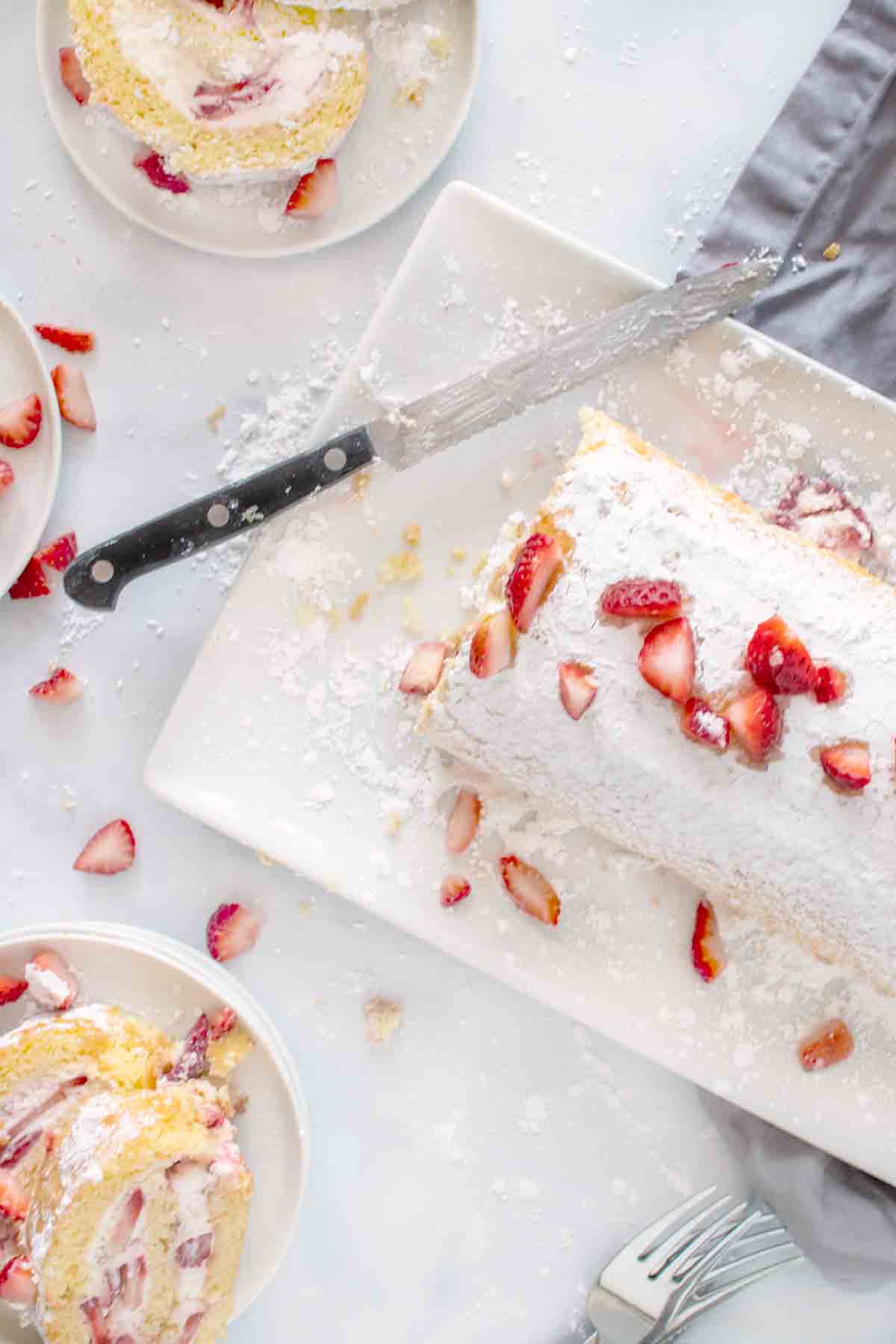 strawberry cake roll on a white platter with a knife.