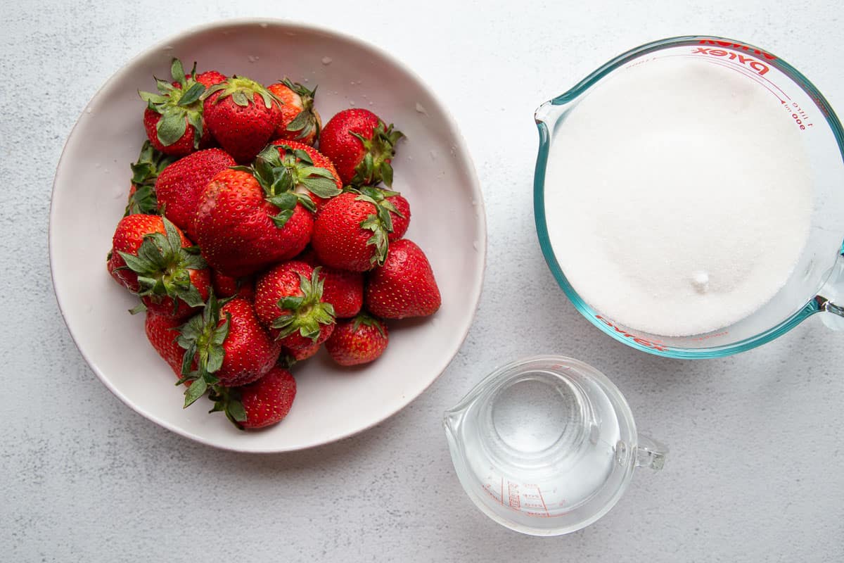 strawberries, sugar, and water on a white table.