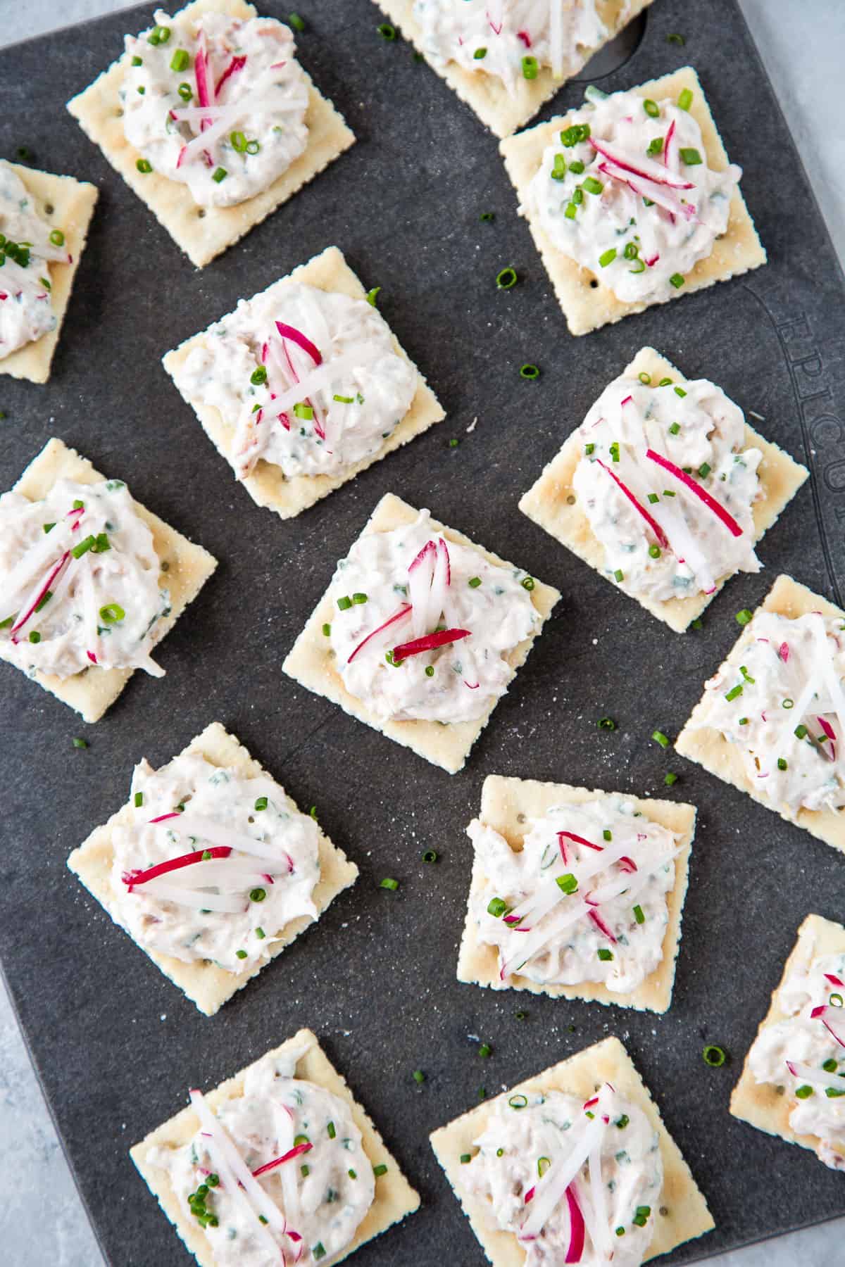 a black cutting board topped with crab dip on saltines.