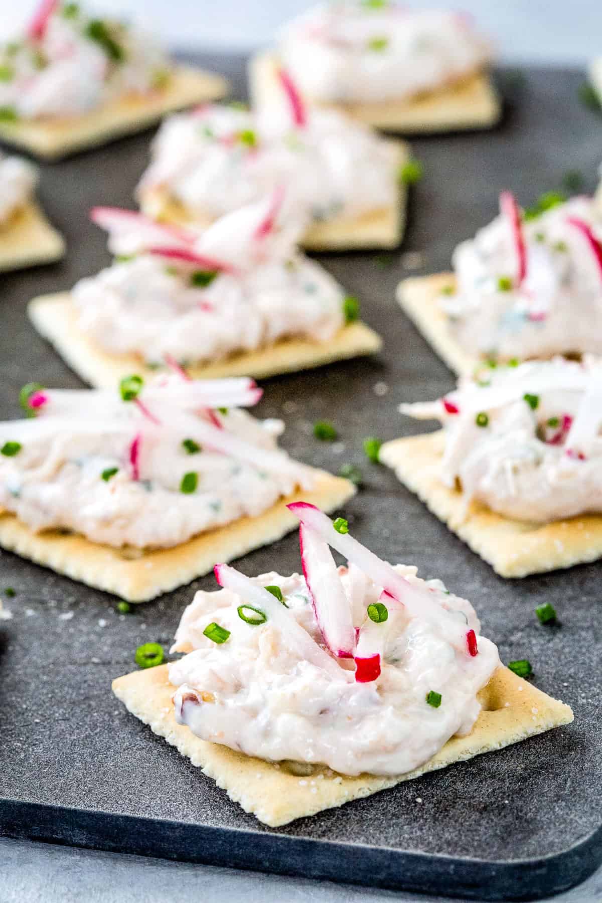 saltine crackers topped with cold crab dip, radishes, and chives.