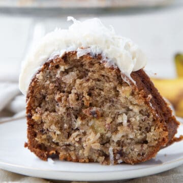 slice of hawaiian cake with cream cheese frosting and coconut on a white plate.