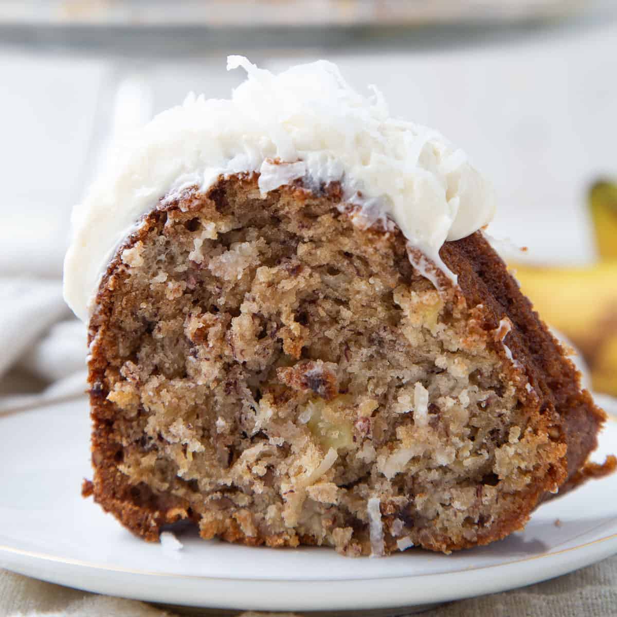 slice of hawaiian cake with cream cheese frosting and coconut on a white plate.