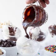hand pouring hot fudge on a scoop of ice cream in a glass parfait dish.