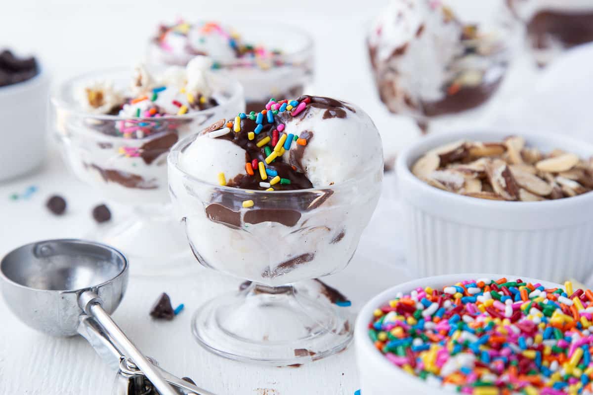 ice cream sundae topped with hot fudge and sprinkles, next to a bowl of rainbow sprinkles.