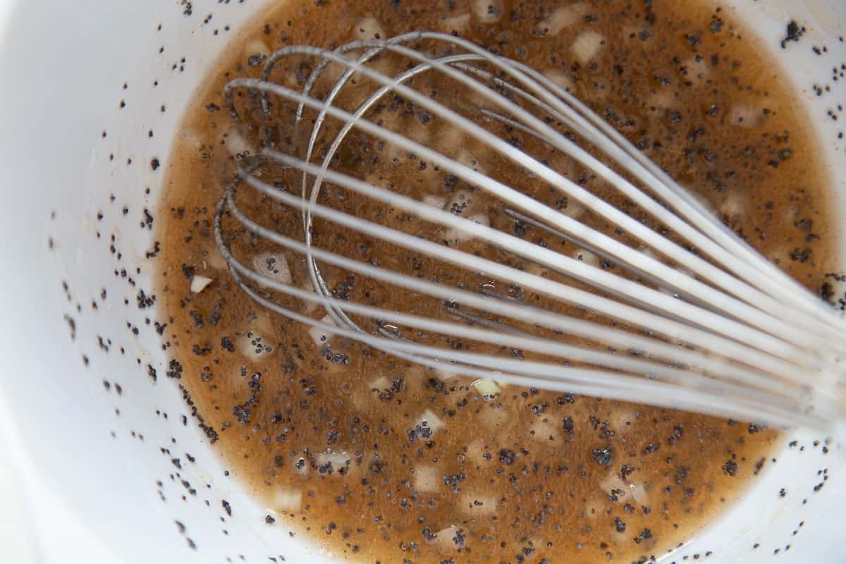 poppy seed vinaigrette in a white bowl with a whisk.