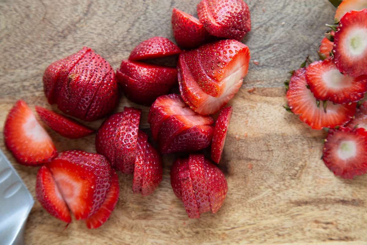 sliced strawberries on a wooden cutting board.