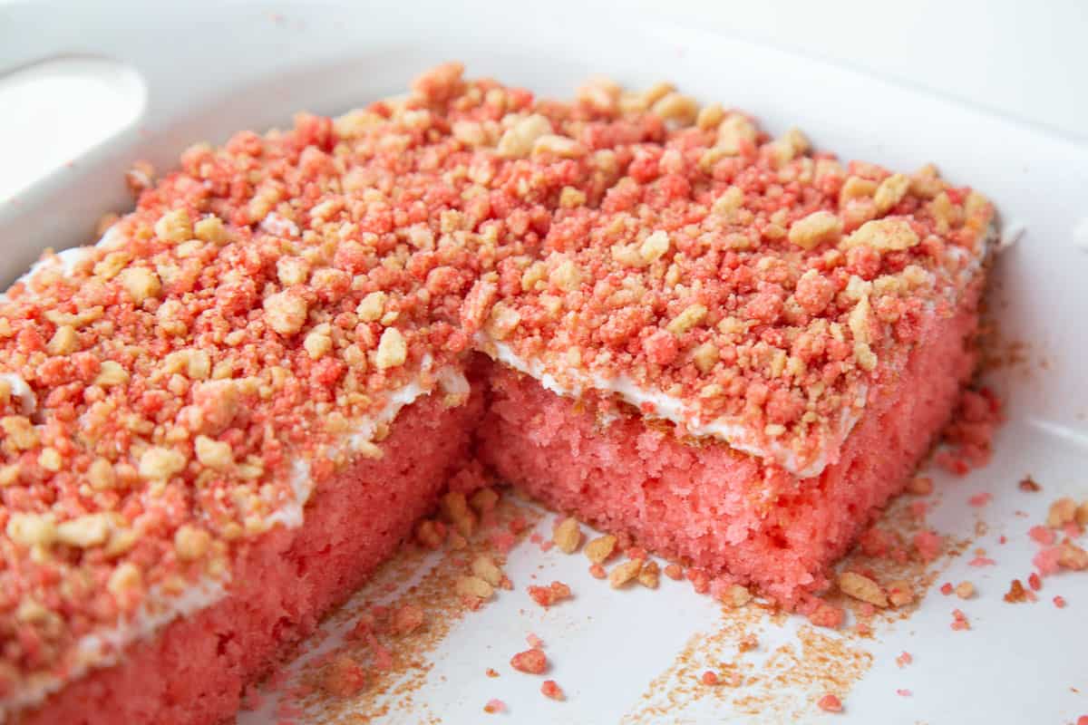 large strawberry crunch cake with slices taken out in a white dish.