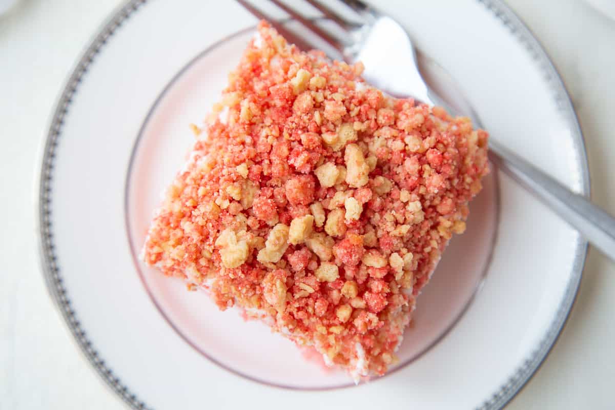 single piece of cake topped with strawberry crunch topping on a white plate with a fork.