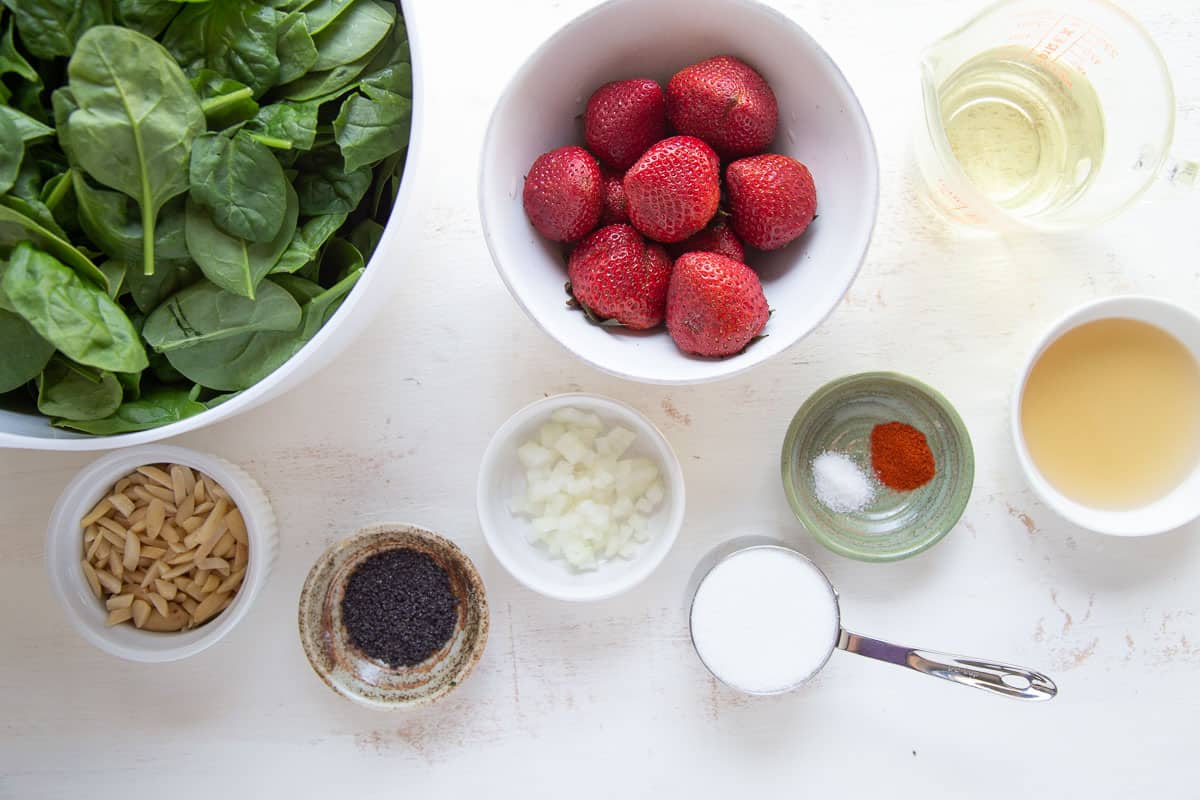 spinach, strawberries, poppy seeds, almonds, and other ingredients on a white table.