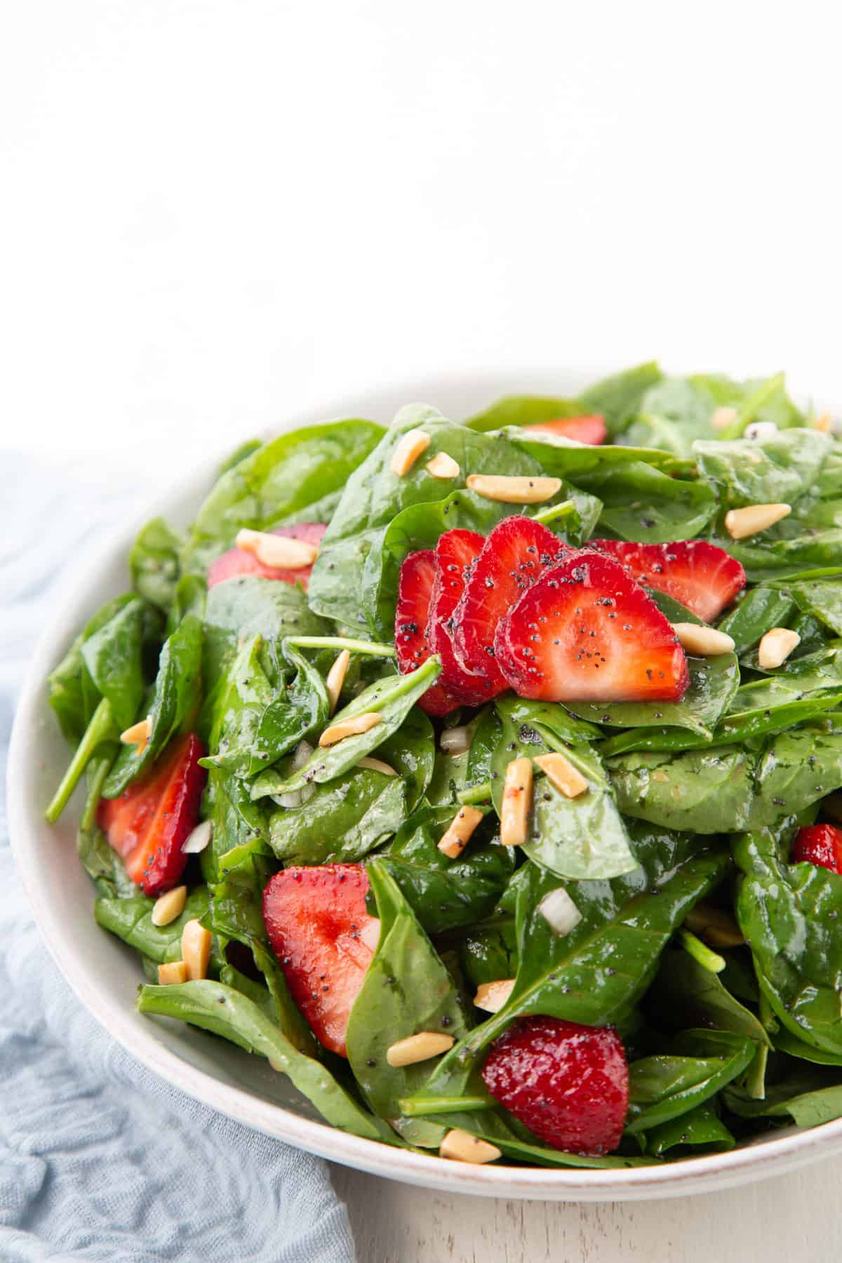 strawberry spinach salad with almonds in a white bowl.