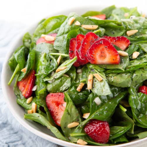 strawberry spinach salad topped with almonds and sliced strawberries in a white bowl.