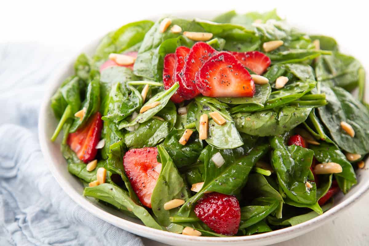 spinach topped with strawberries and slivered almonds in a white bowl.