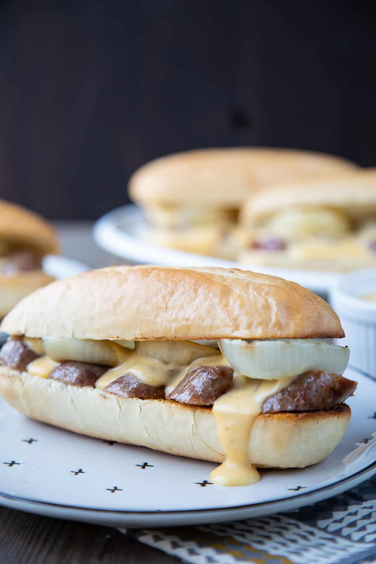 beer brat on a plate in a bun with onions and cheese sauce dripping out.