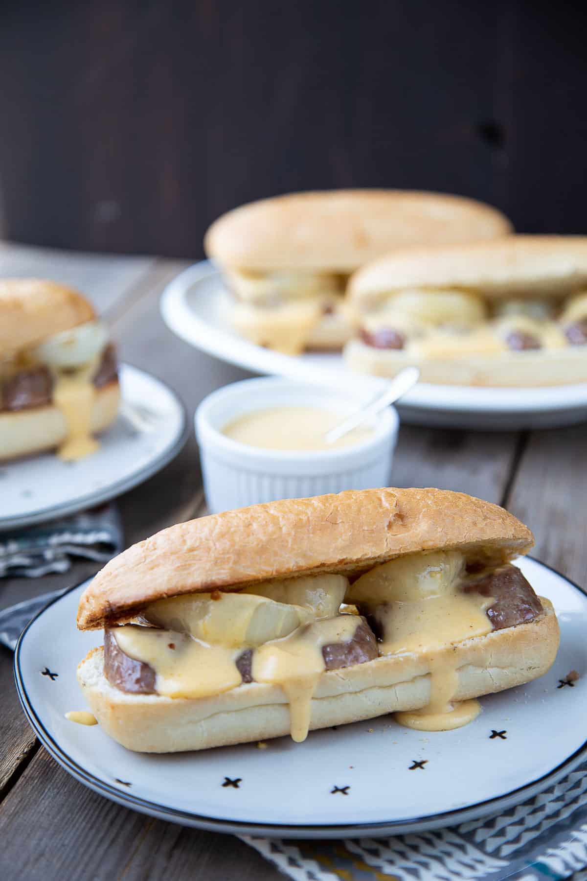 plate with a hoagie roll stuffed with brat slices, onions, and cheese sauce.