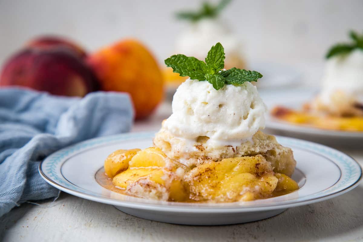 peach cobbler made with bisquick on a white plate, topped with vanilla ice cream and a mint sprig.
