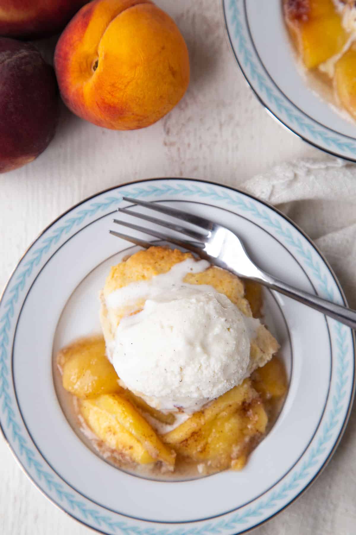 scoop of bisquick peach cobbler on a blue and white plate topped with vanilla ice cream.
