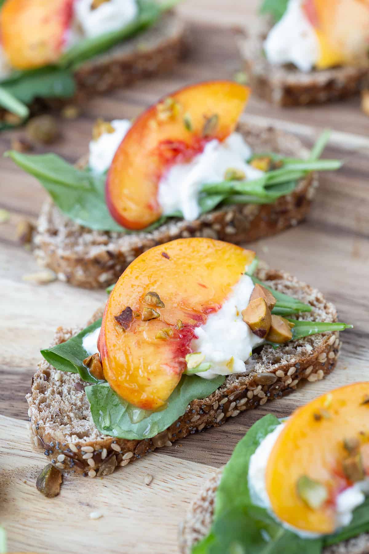 arugula, a peach slice, burrata, and pistachios on a whole grain toast.