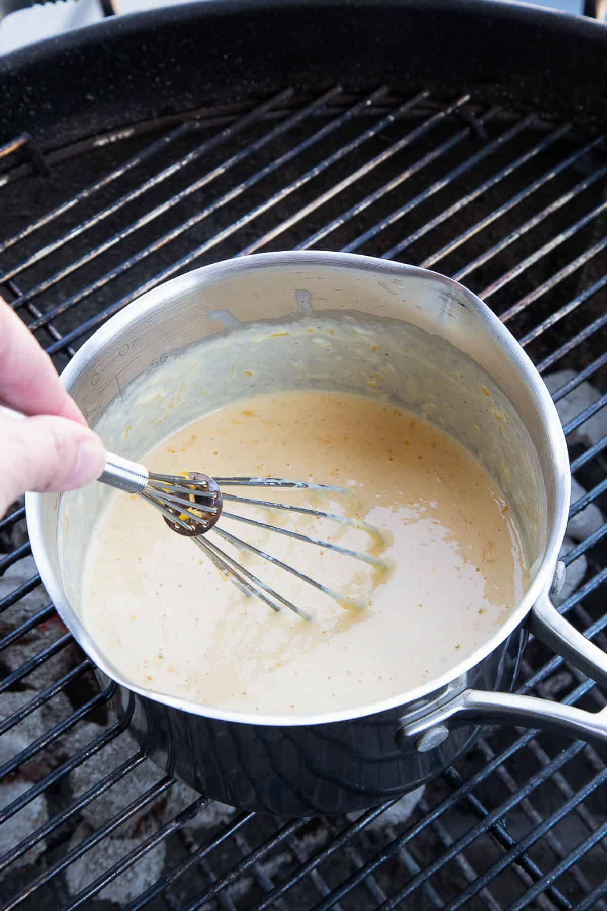 hand whisking cheese sauce in a saucepan on a grill.