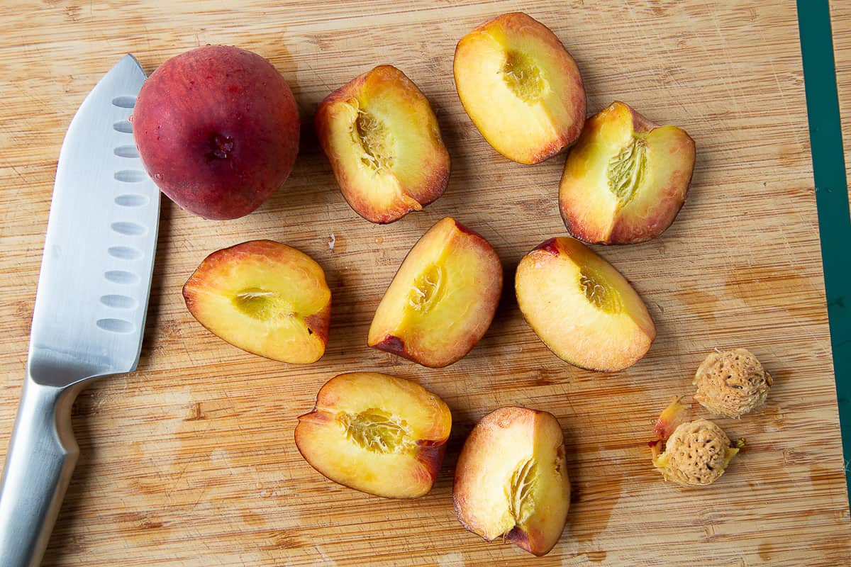 quartered peaches and a knife on a wooden cutting board.