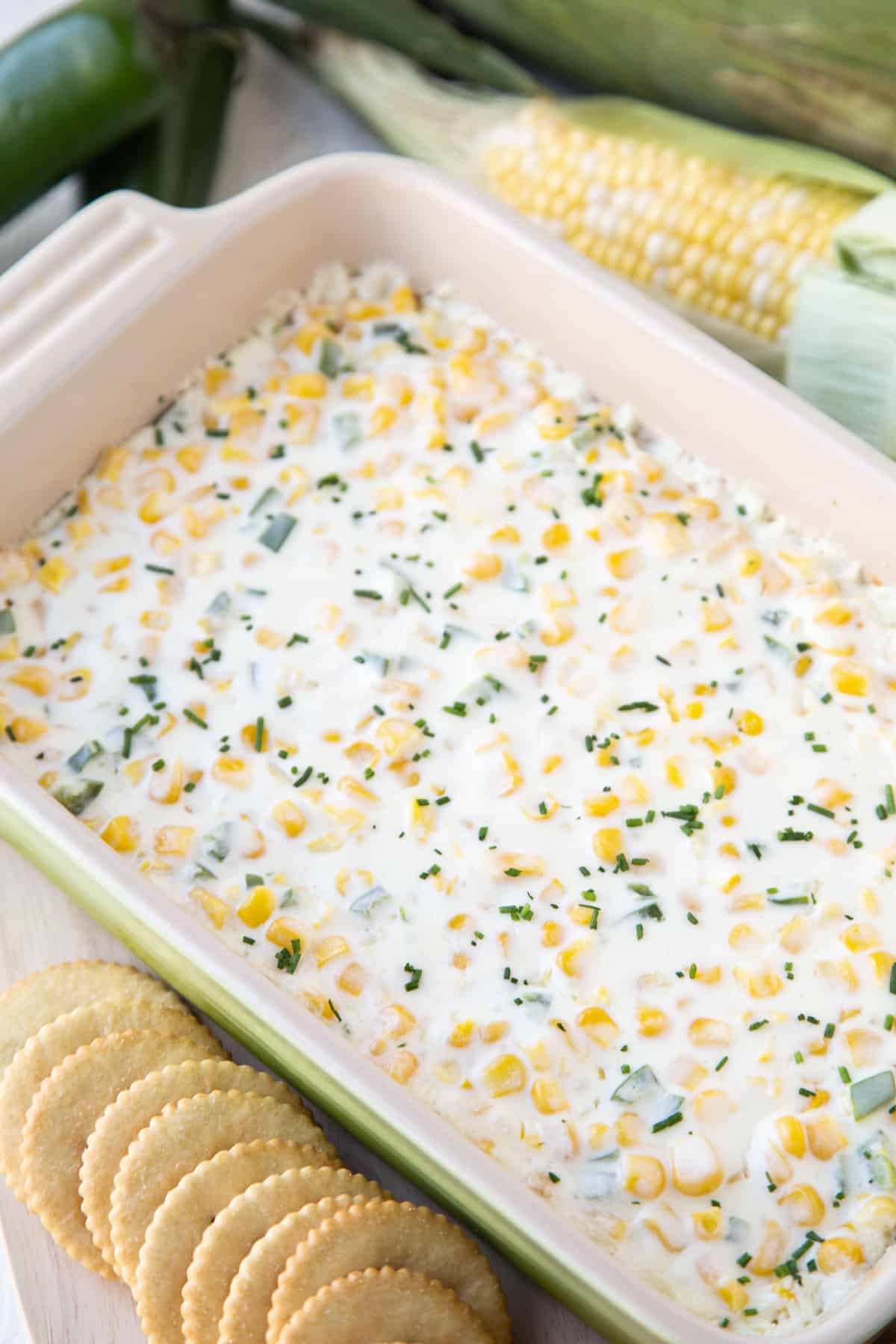 corn dip in a casserole dish next to a row of crackers.