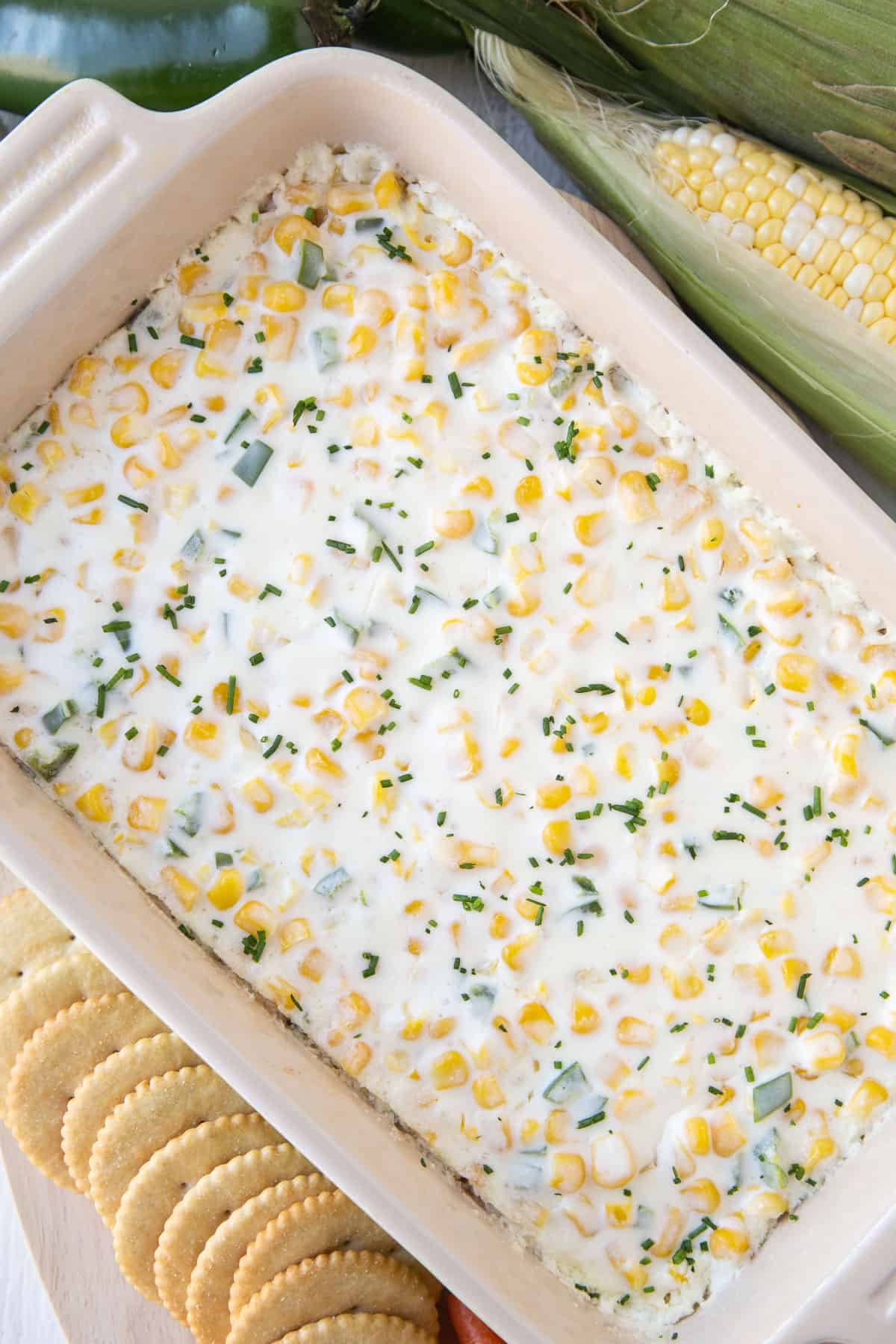 casserole dish filled with cream cheese corn dip next to a row of crackers.