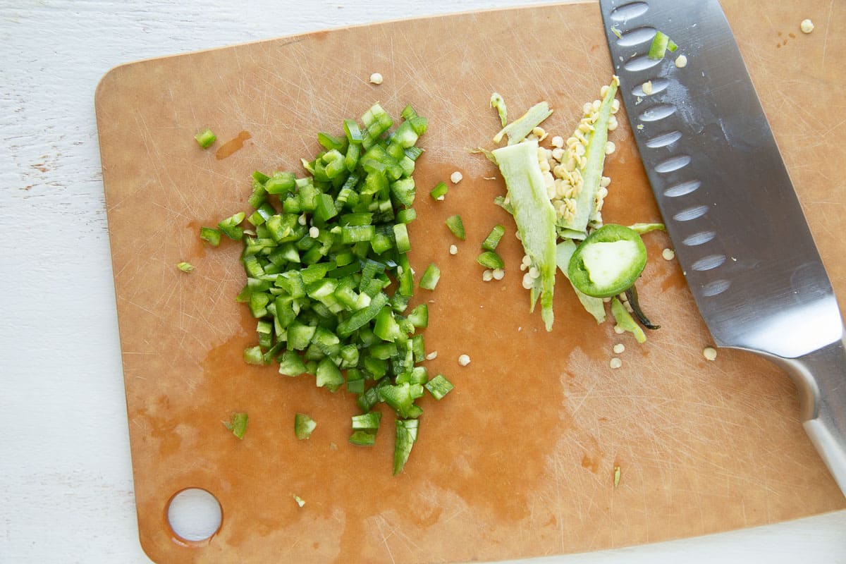 chopped jalapeño on a wooden cutting board next to a knife.