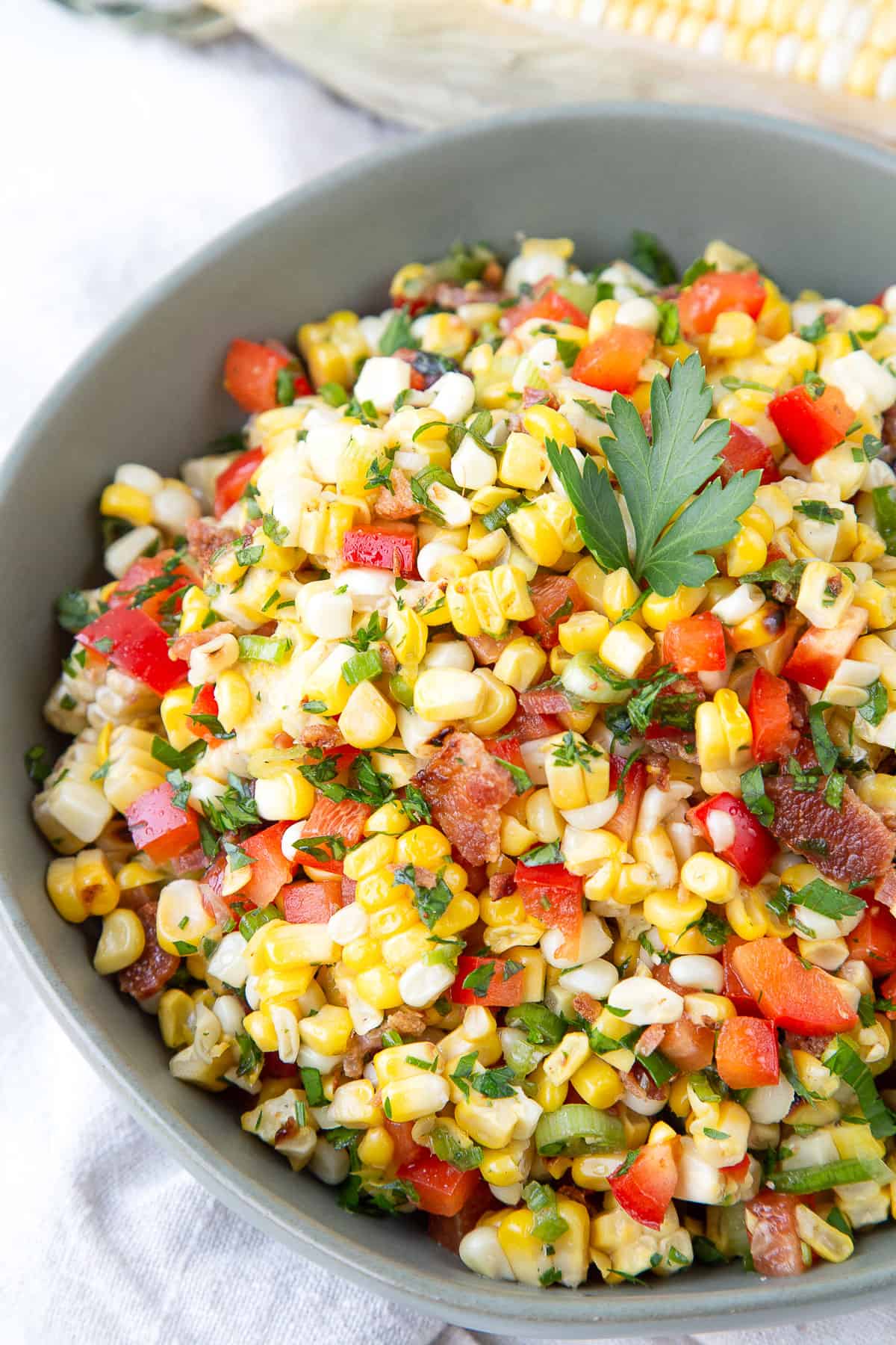 grilled corn salad with bacon in a green bowl, garnished with parsley.