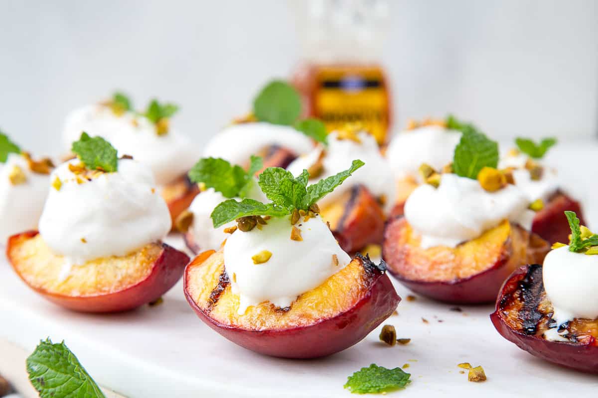 grilled peach quarters on a white platter, topped with whipped cream and mint sprigs.