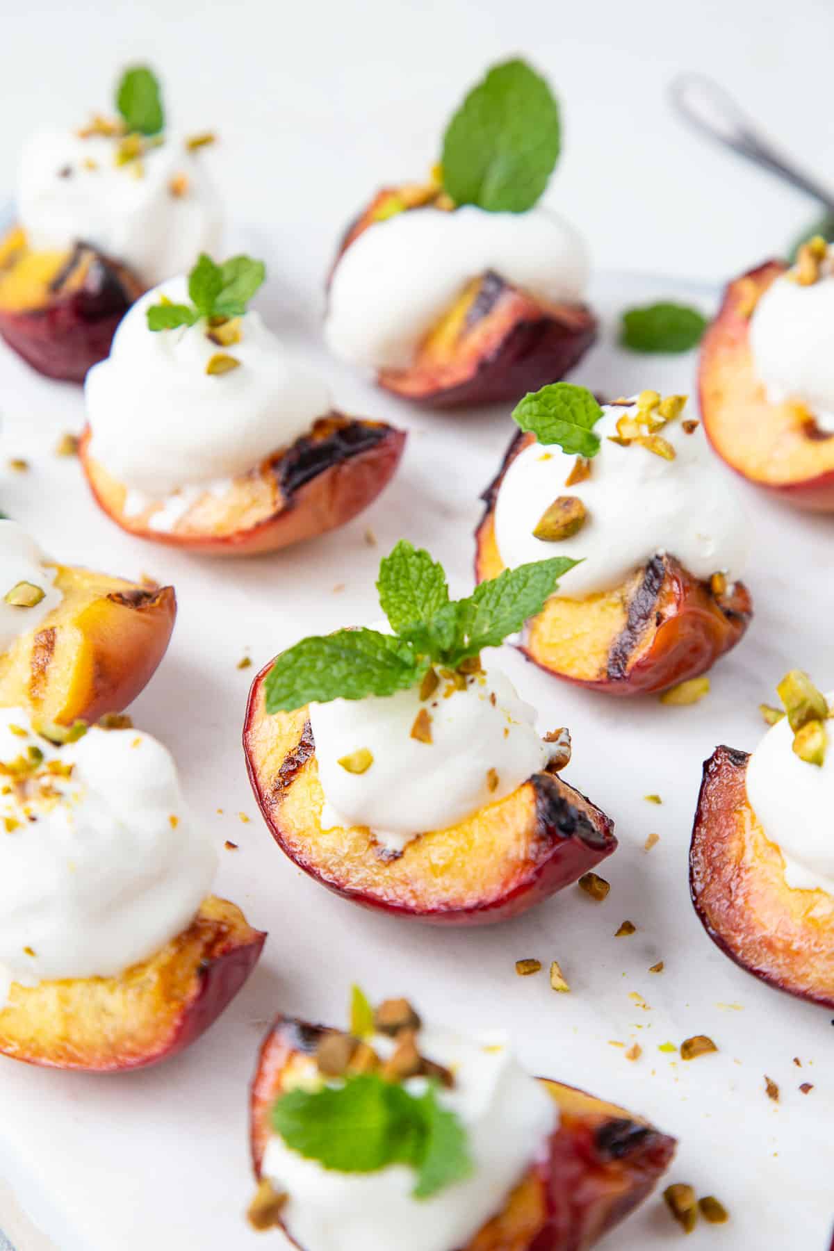 grilled peach quarters with whipped cream and mint on a white platter.