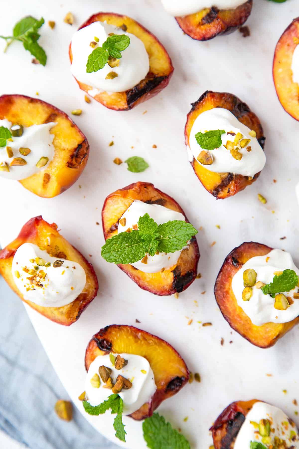 grilled peach quarters on a white platter, topped with whipped cream and mint sprigs.