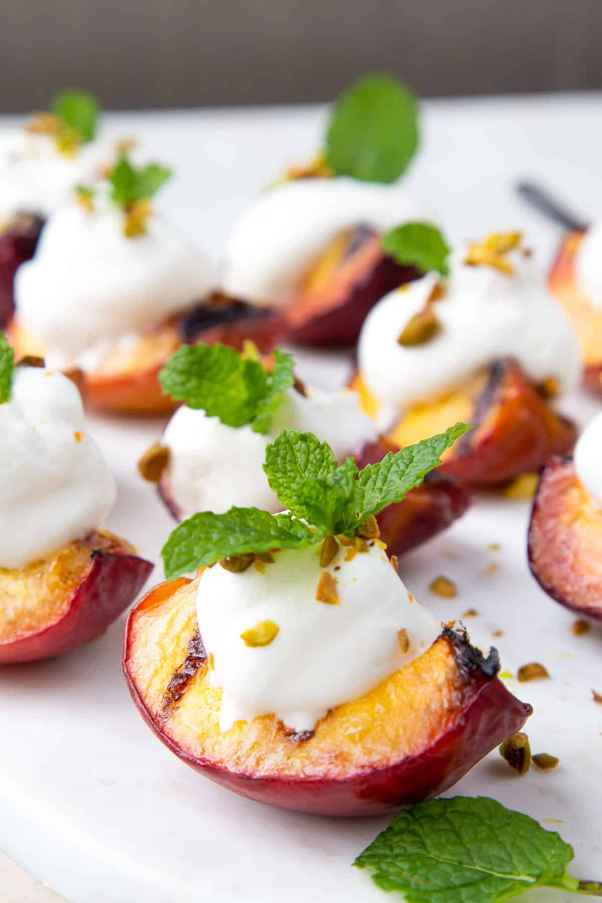 grilled peach quarters on a white platter, topped with whipped cream and mint sprigs.