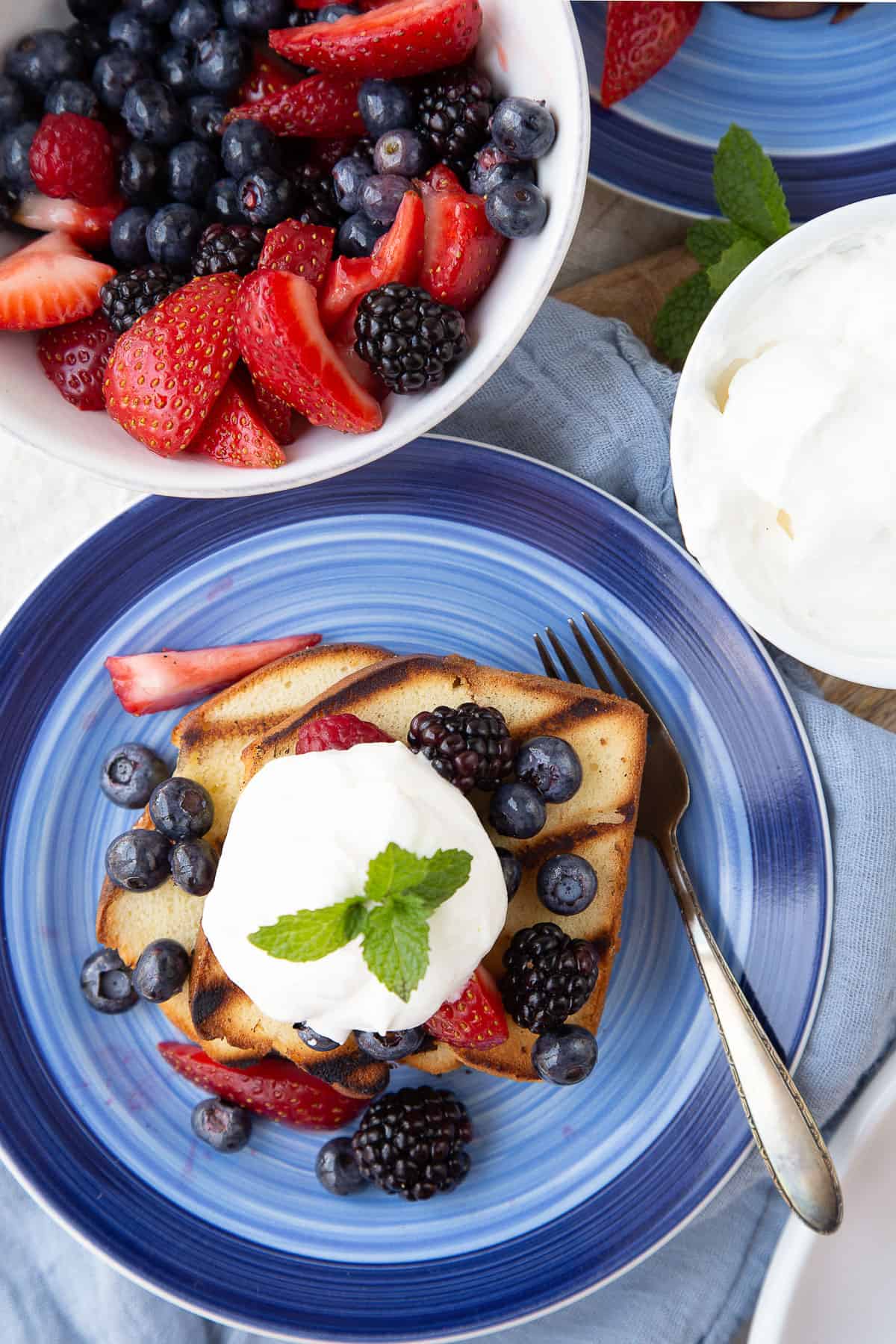 grilled pound cake with berries and whipped cream on a blue plate.