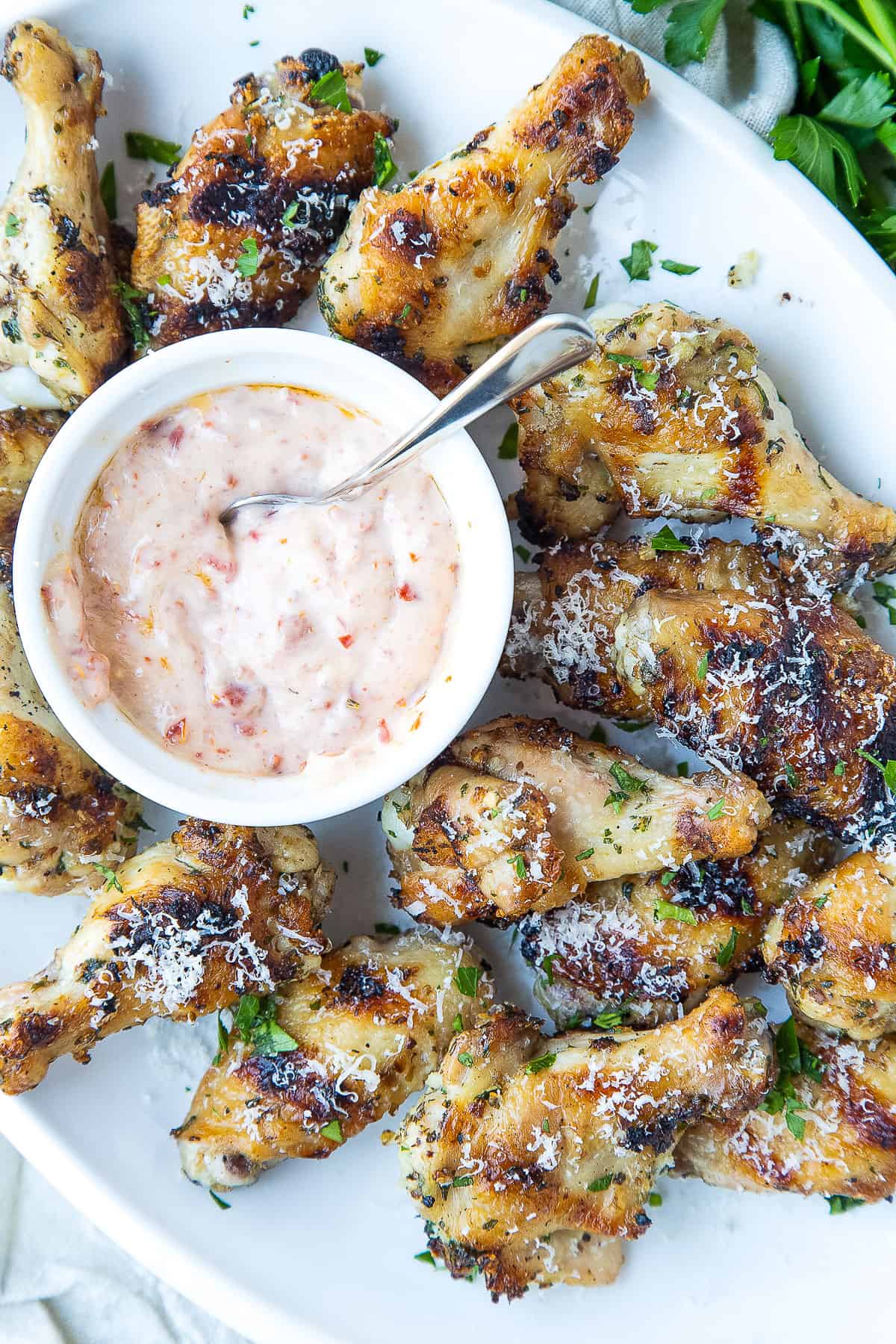 chicken wings stacked on a white platter with a bowl of orange dipping sauce.