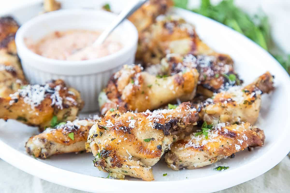 grilled wings on a white platter with an orange dipping sauce bowl.