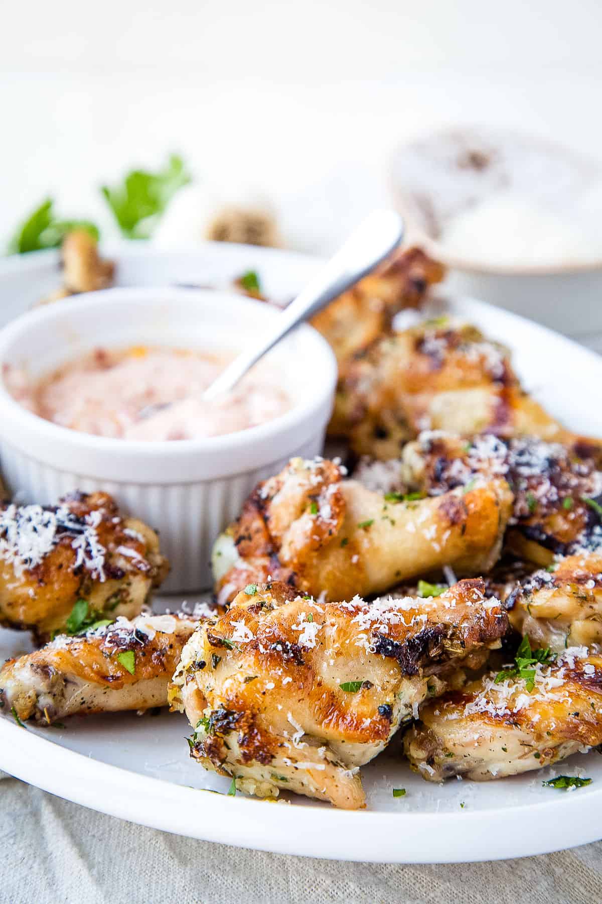 garlic and herb chicken wings on a white platter with a bowl of chipotle dipping sauce.