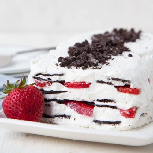 icebox cake with strawberries on a white platter with a whole strawberry.