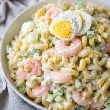 macaroni salad with shrimp topped with hard boiled eggs in a white bowl.