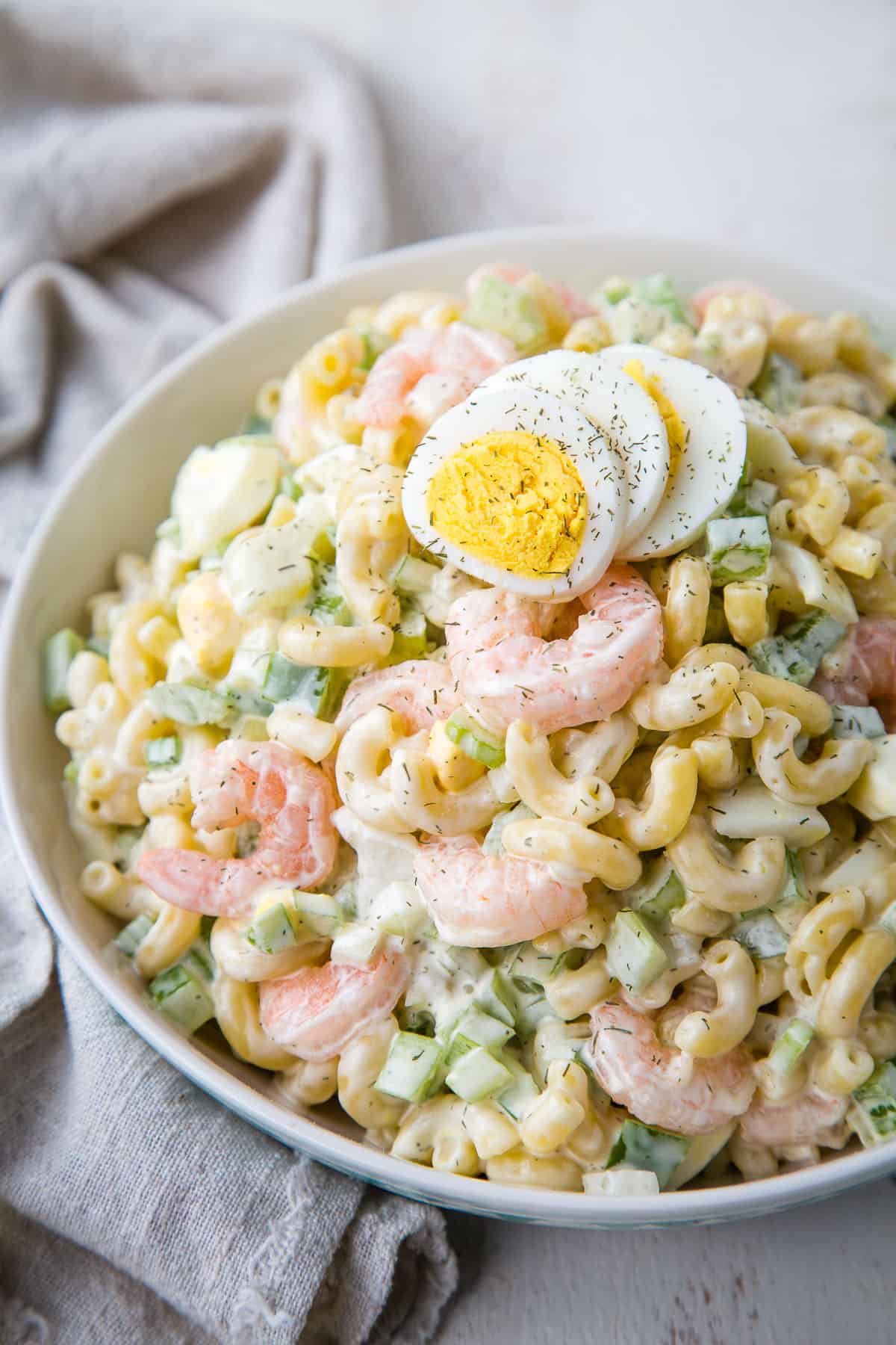macaroni salad with shrimp in a white bowl, topped with hard boiled egg slices.