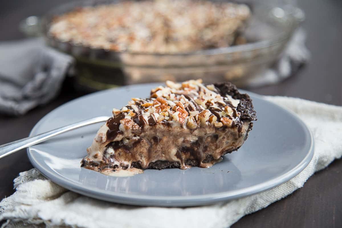 slice of ice cream pie on a gray plate topped with fudge sauce and pecans.