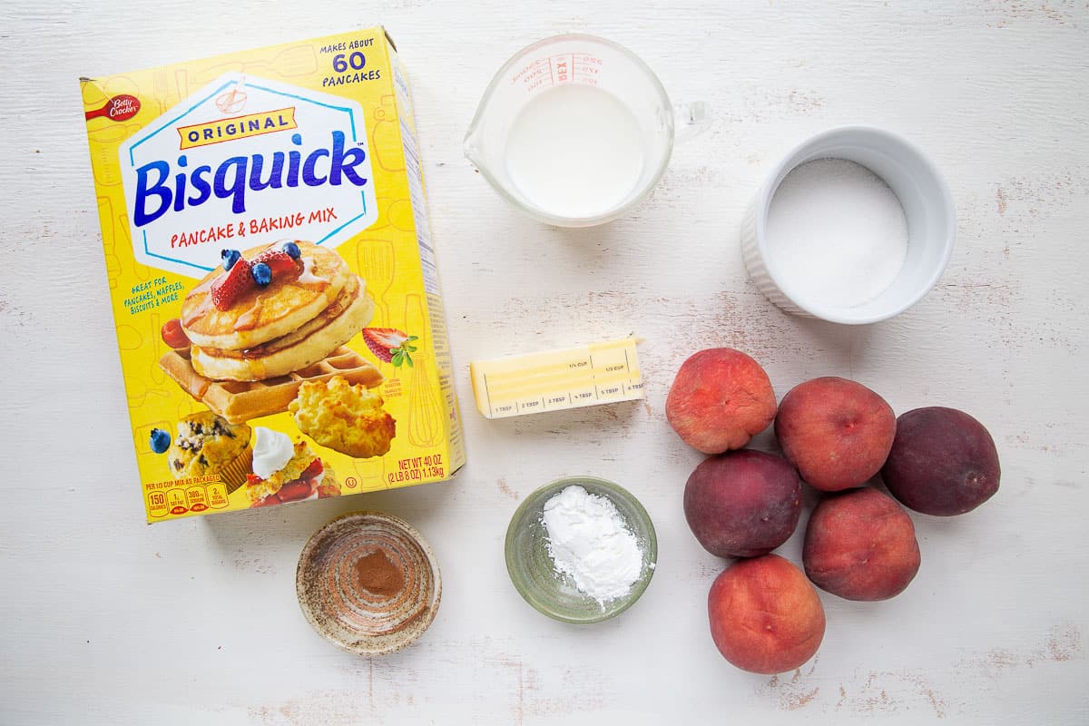 bisquick, peaches, butter, and other ingredients on a white table.