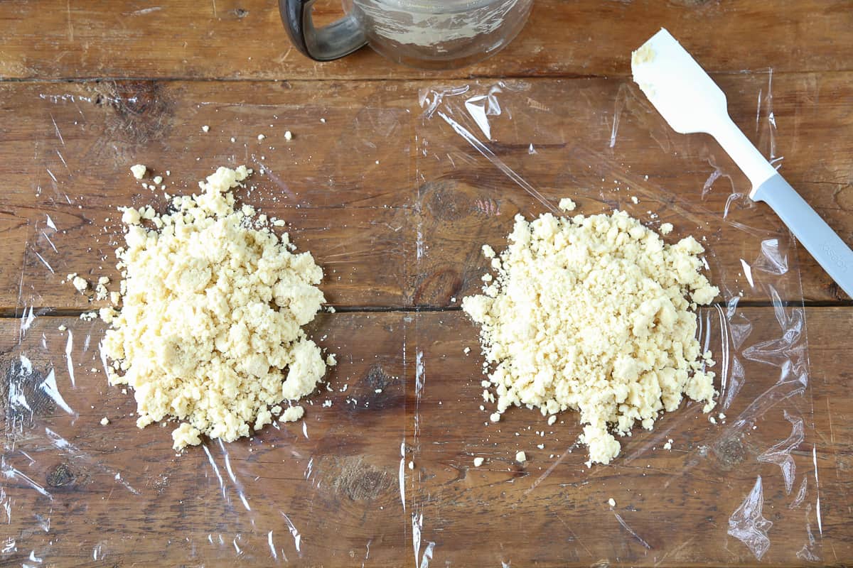 two piles of crumbly pie dough on pieces of plastic wrap.