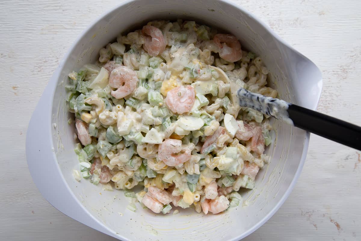 macaroni salad with shrimp in a white bowl with a spatula. 