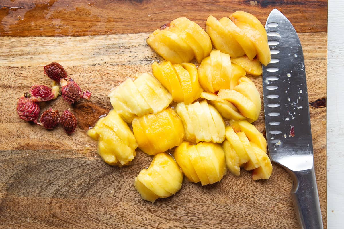 peeled and sliced peaches on a wooden cutting board.